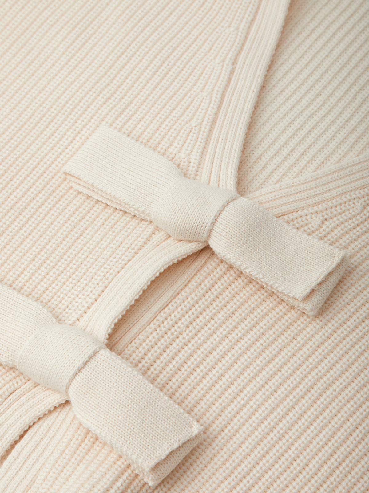 Close-up of a beige ribbed sweater with a bow detail.