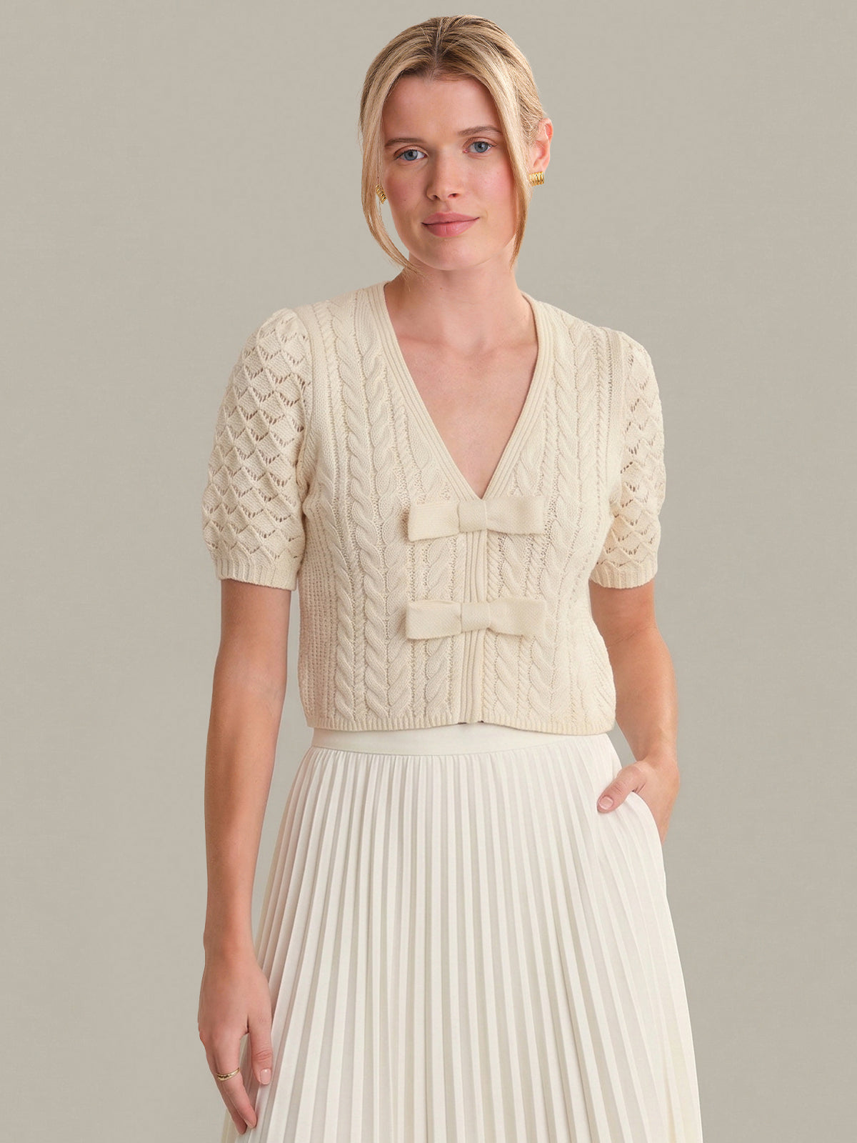 Woman wearing a cream-colored cable knit cardigan over a white dress against a neutral background