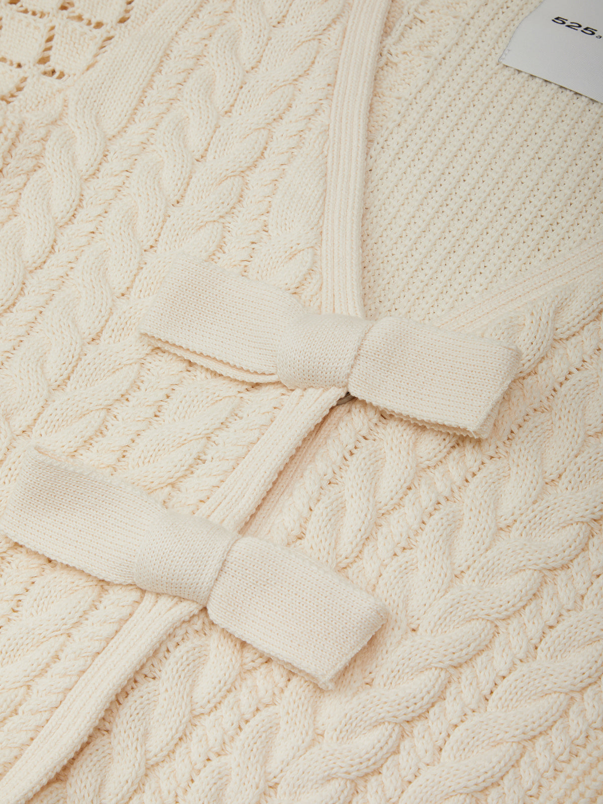 Close-up of a cream-colored cable knit sweater with a bow detail.