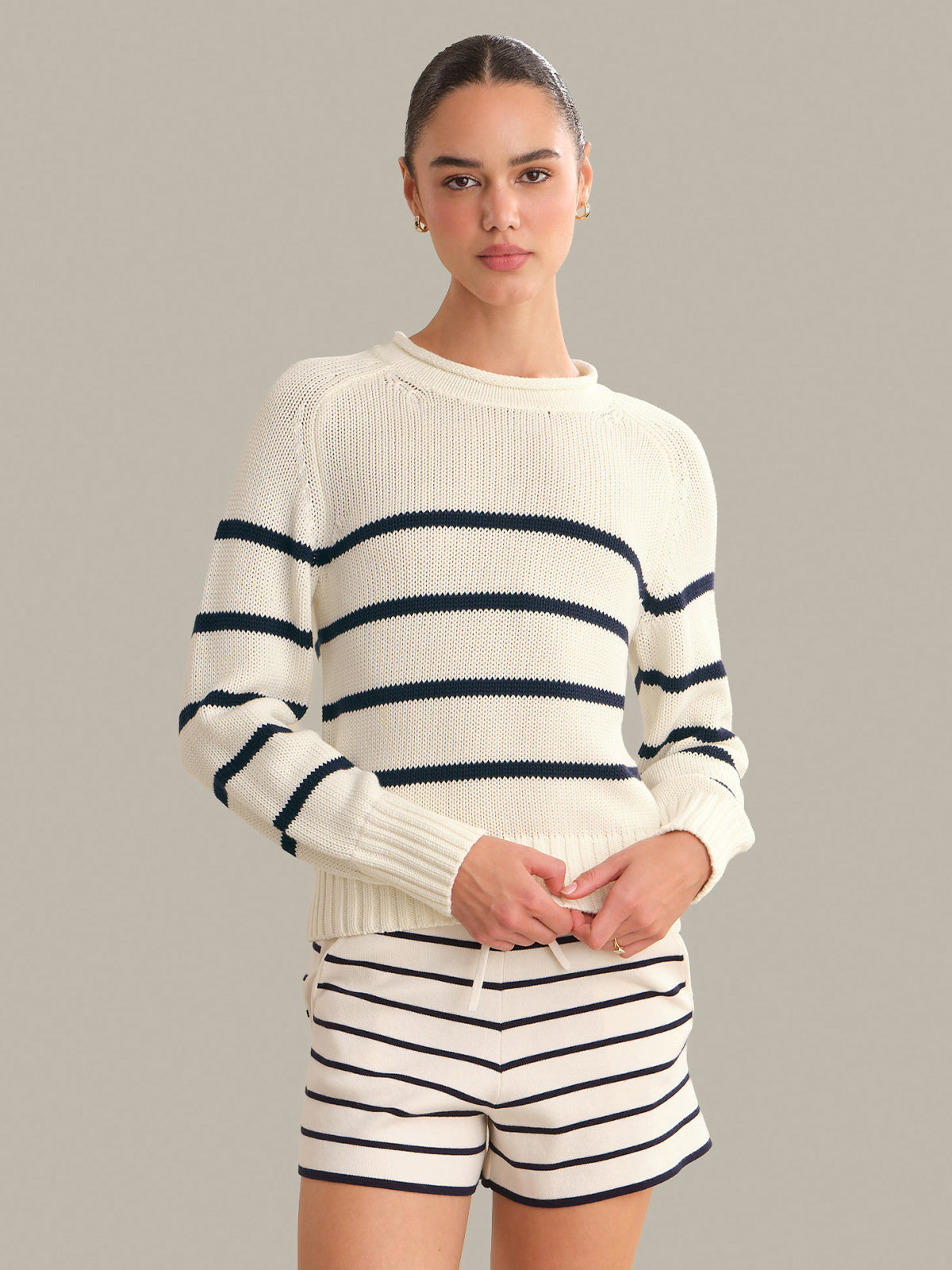 Woman wearing a white sweater with navy stripes and matching shorts on a gray background