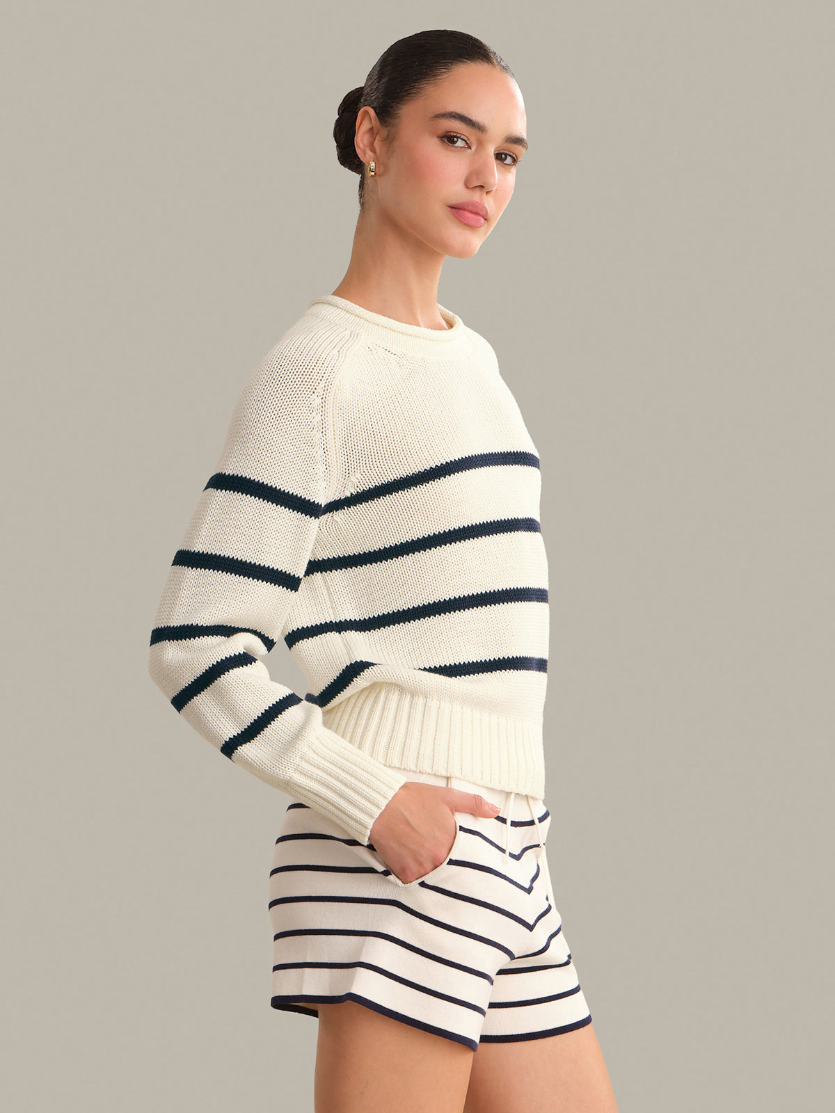 Woman wearing a white sweater with blue stripes and matching shorts against a gray background