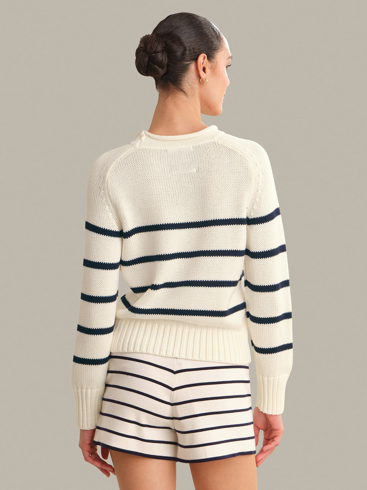 Woman wearing a cream sweater with navy stripes and matching shorts on a gray background