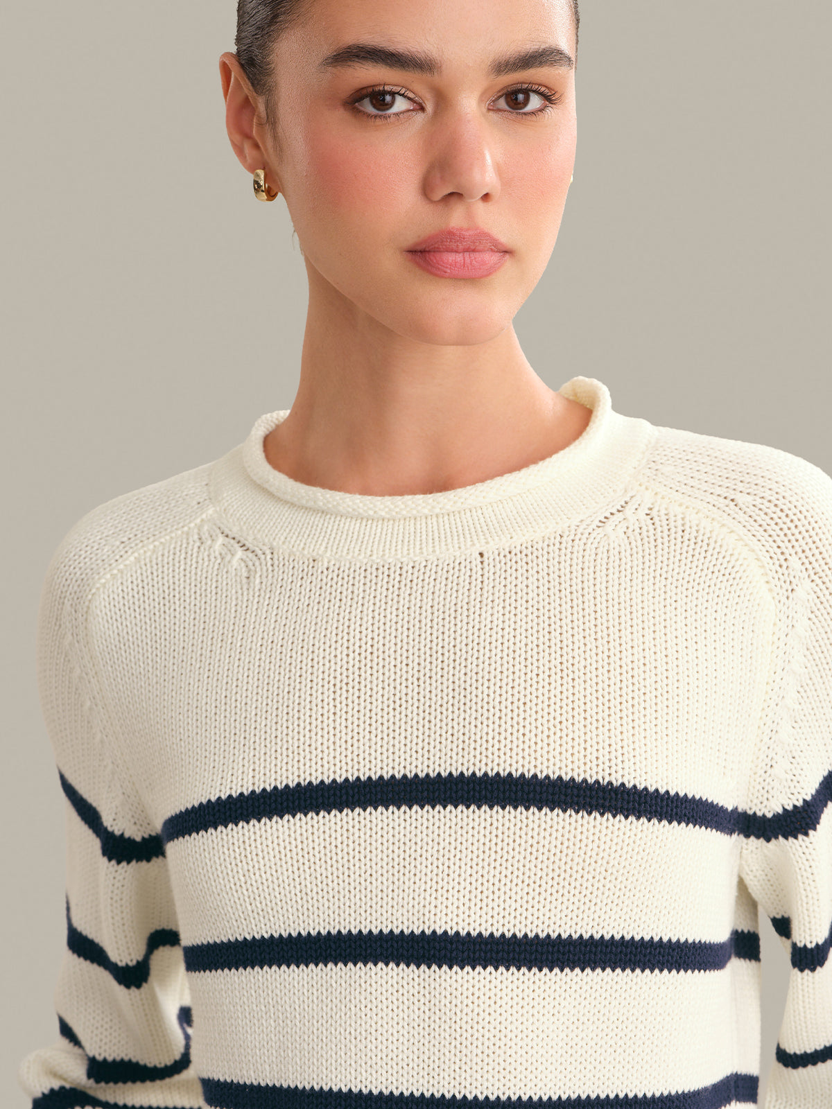 Woman wearing a white sweater with navy stripes against a neutral background