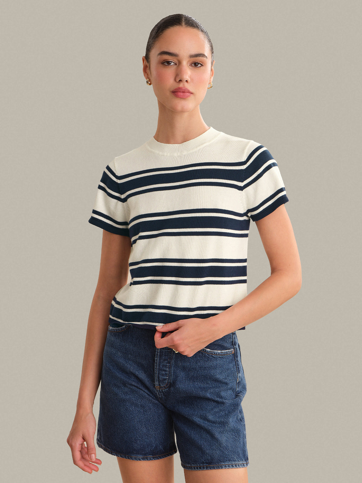 Person wearing a striped top and denim shorts against a plain background