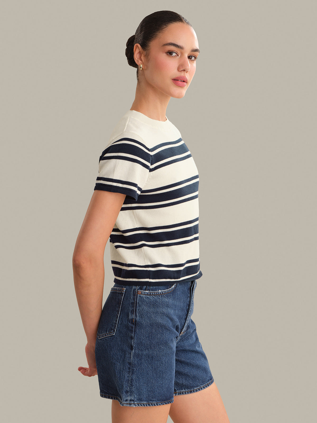 Woman wearing a striped top and denim shorts on a plain background