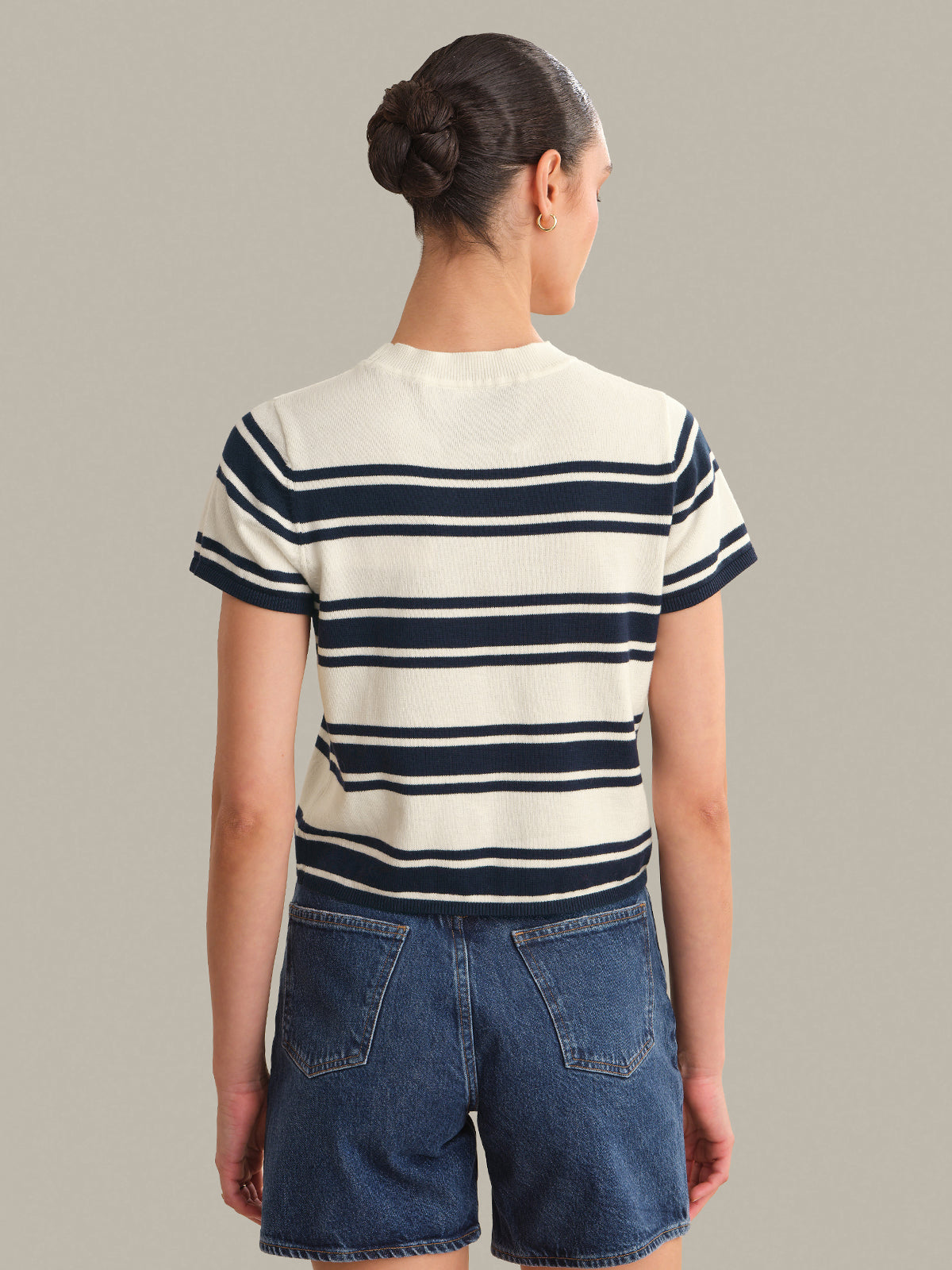 Person wearing a striped top and denim shorts on a plain background