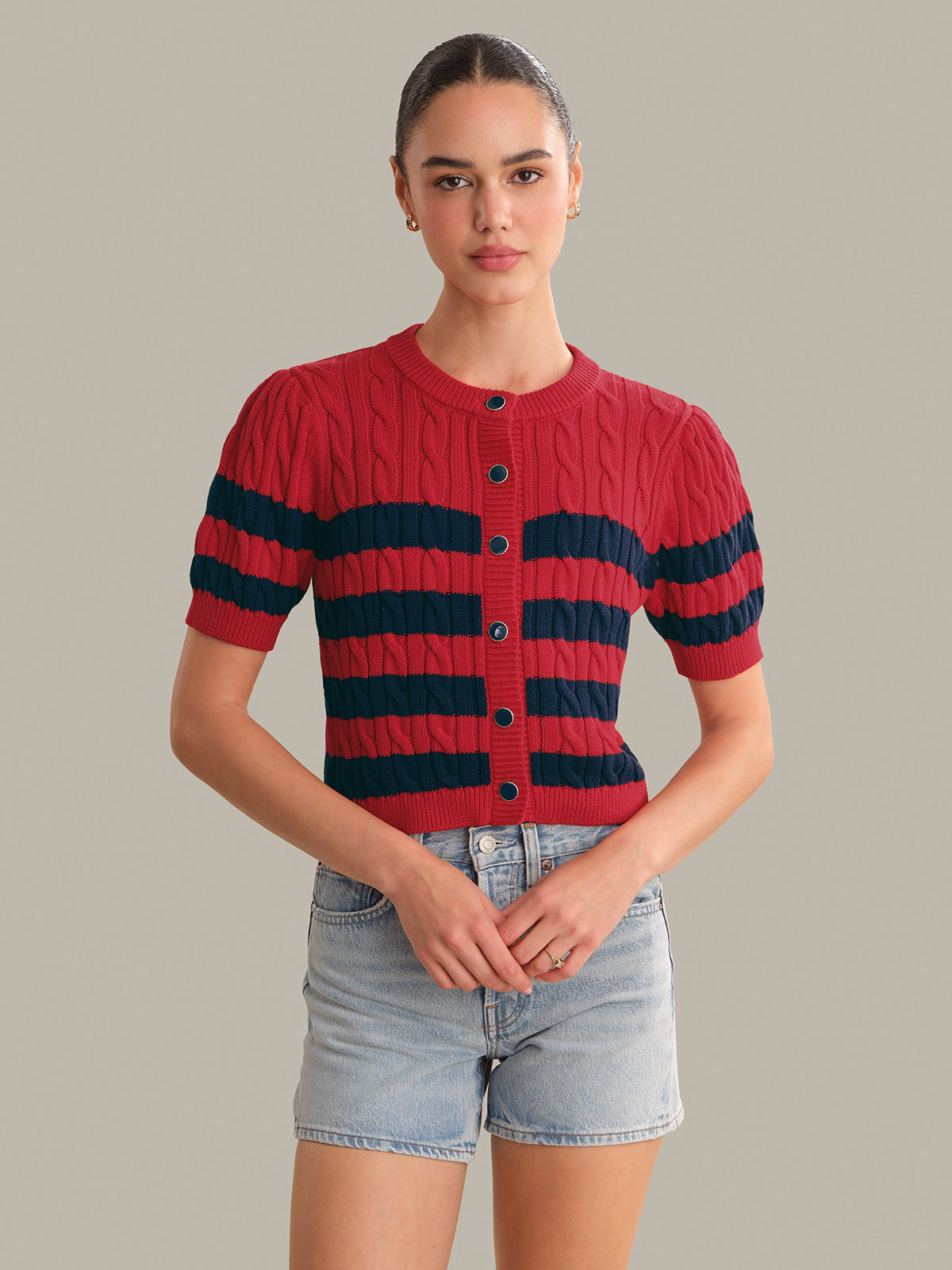 Woman wearing a red and navy striped sweater with denim shorts on a gray background