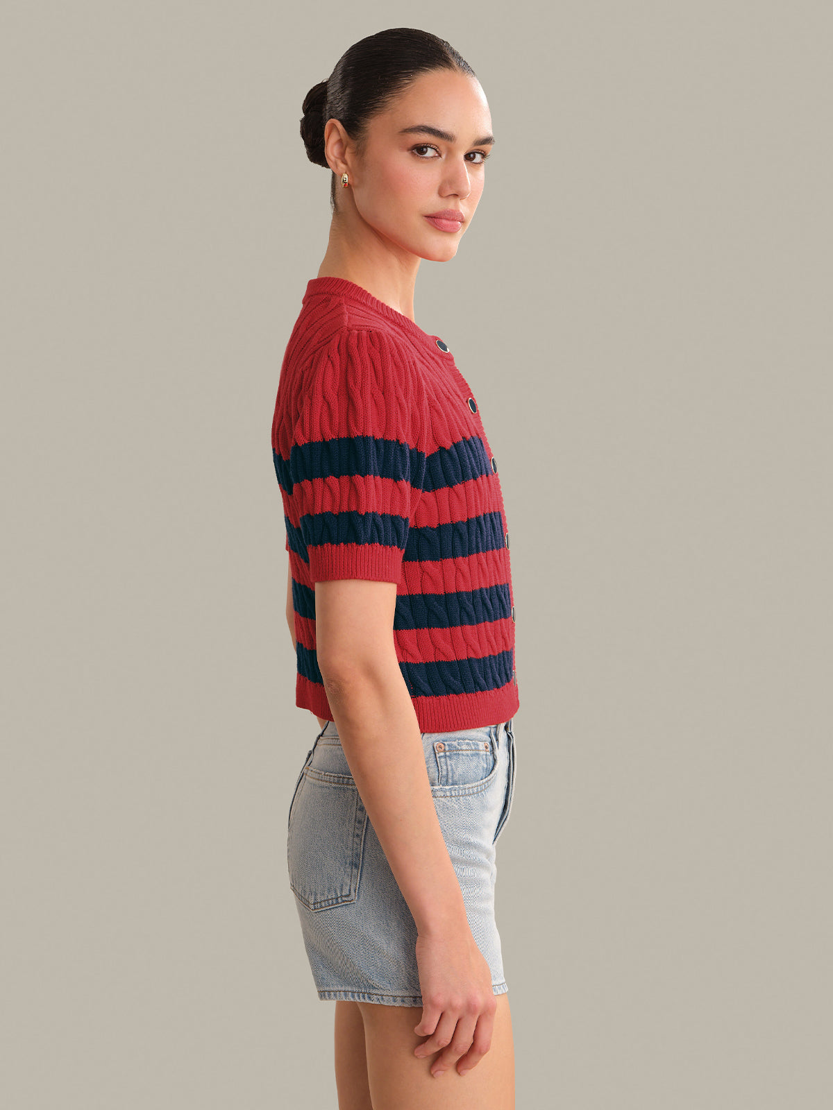 Woman wearing a red and navy striped sweater with denim shorts on a gray background