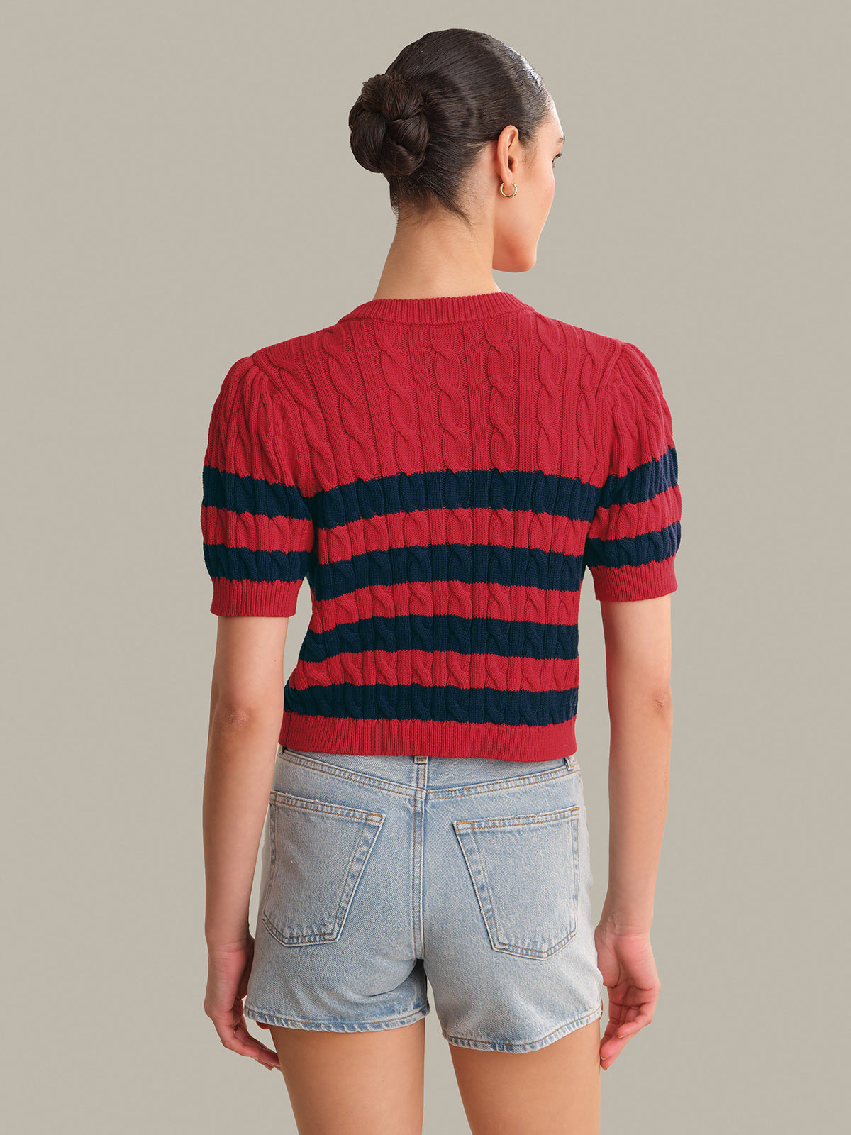 Person wearing a red and navy striped sweater with denim shorts on a neutral background