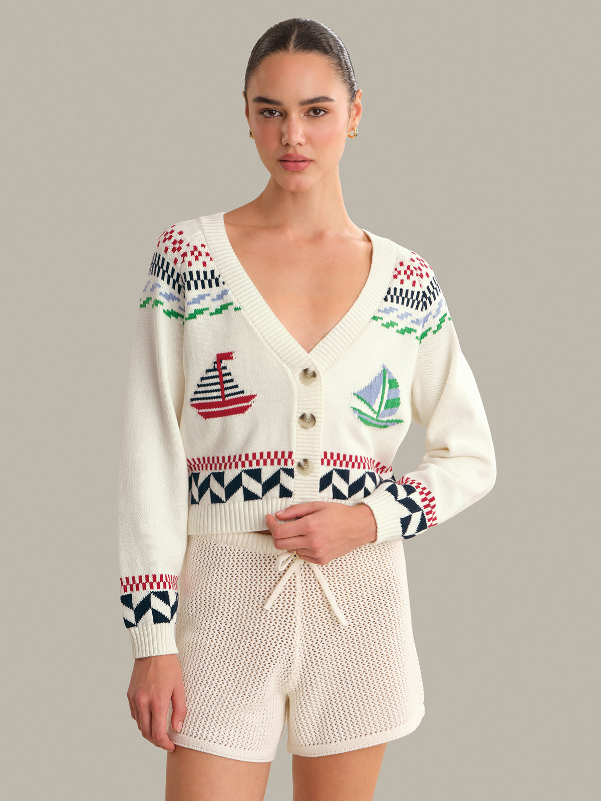 Woman wearing a patterned cardigan with sailboat designs on a plain background