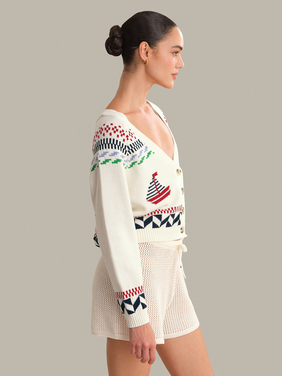 Woman wearing a patterned white cardigan with colorful designs on a plain background