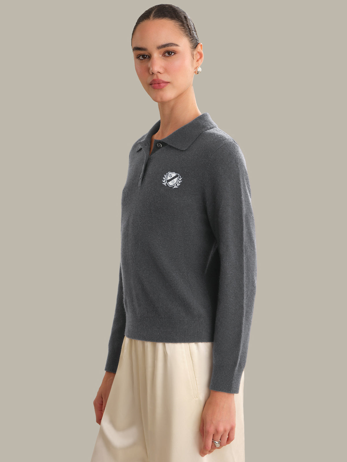Woman wearing a dark gray sweater with a logo on a plain background