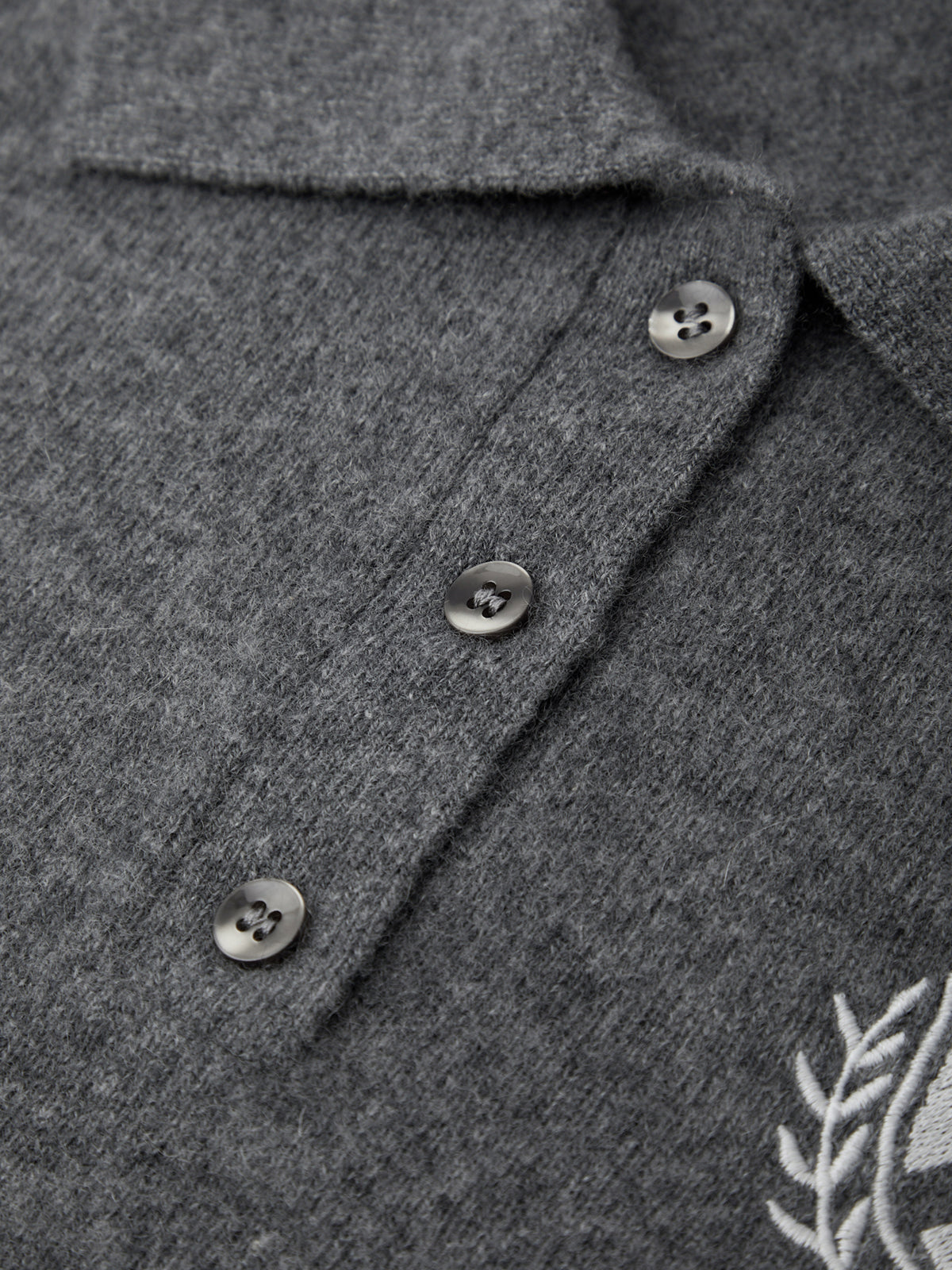 Close-up of a gray textured shirt with buttons and a leaf design on a dark background