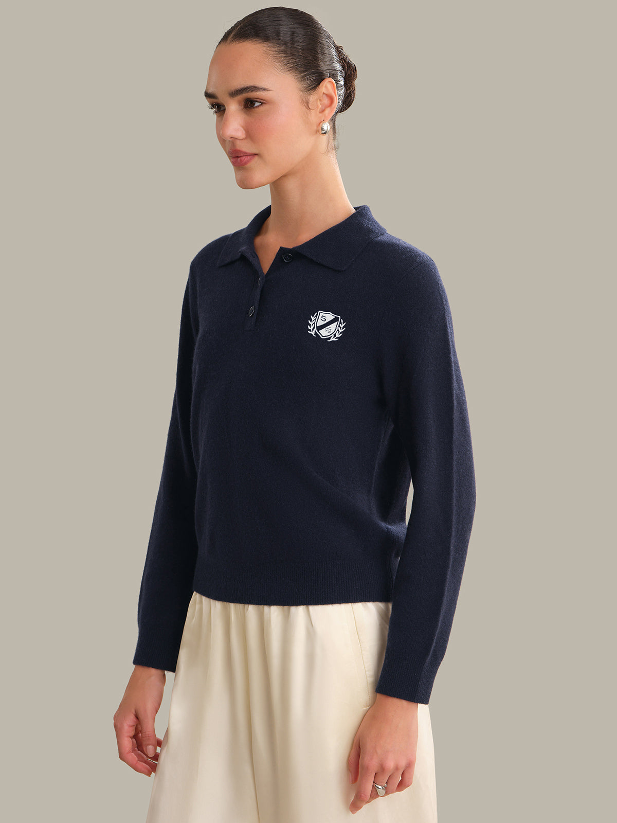 Woman wearing a navy long-sleeve polo shirt with a logo on a neutral background
