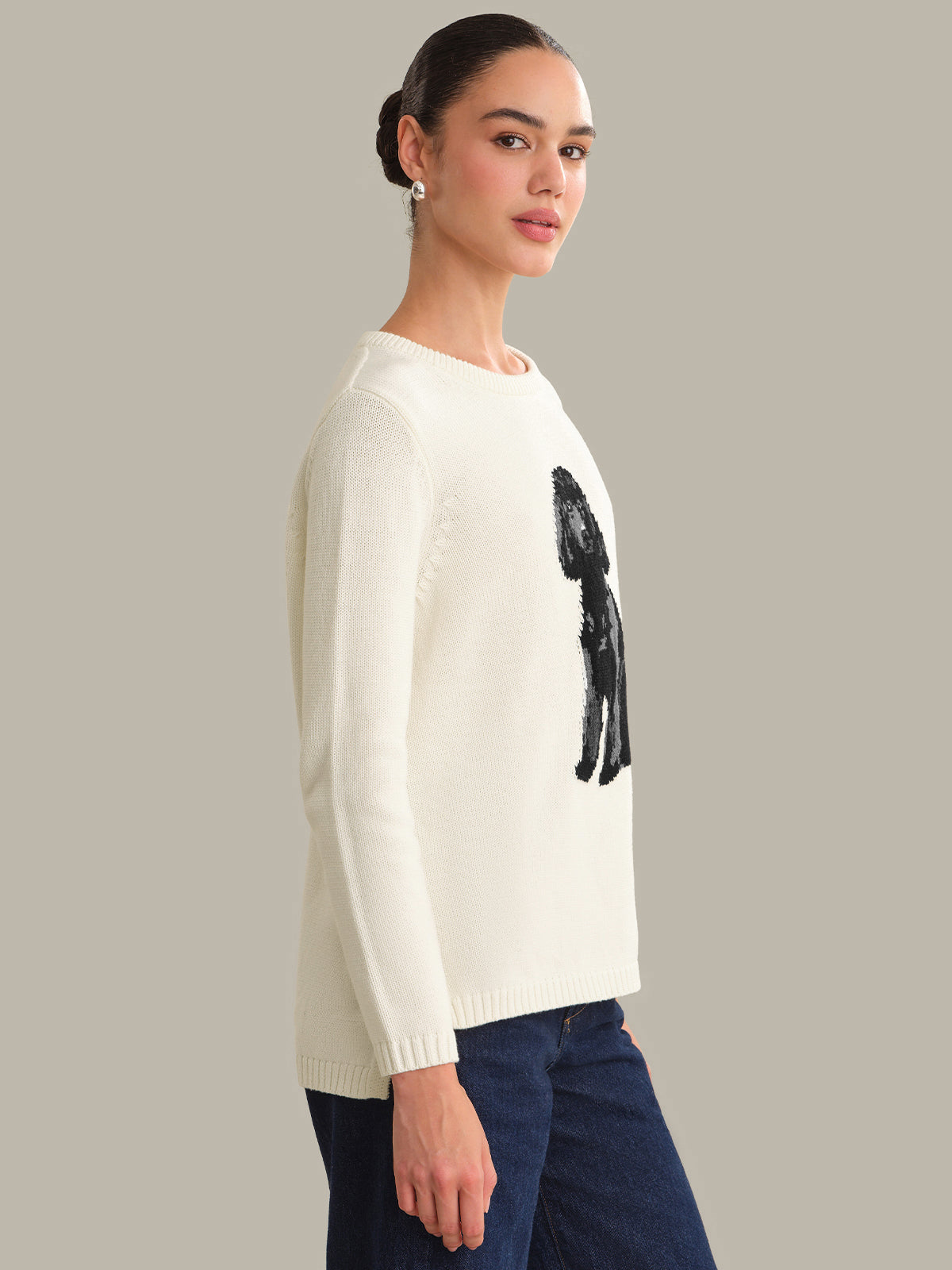 Woman wearing a cream sweater with a black graphic design on a plain background
