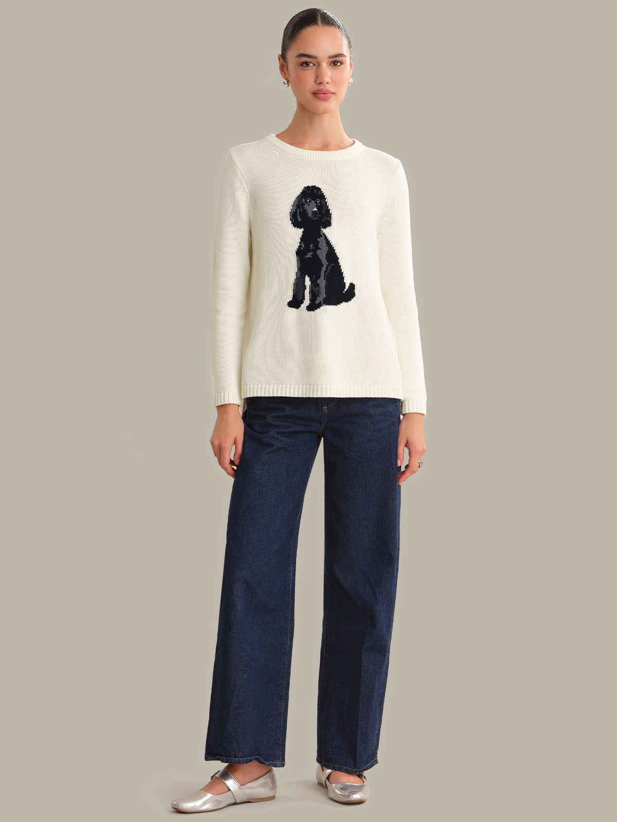 Woman wearing a white sweater with a black dog design and dark blue pants on a gray background