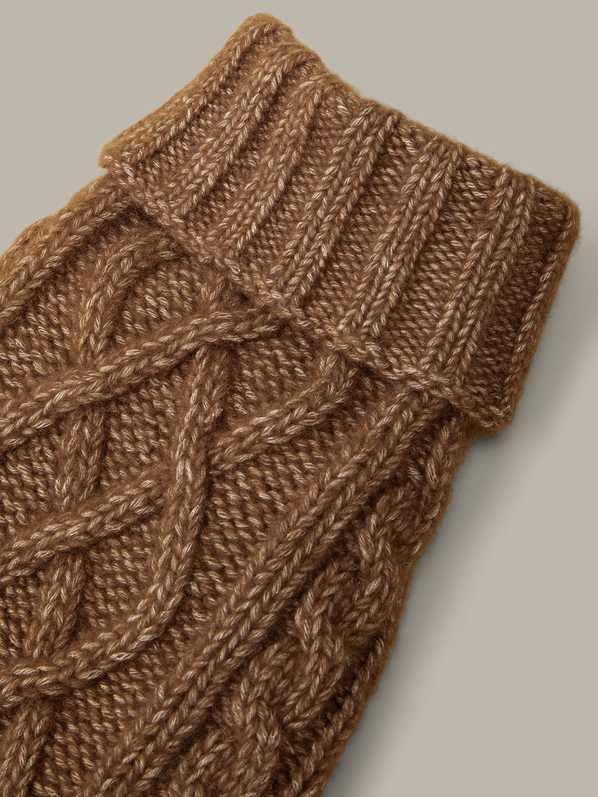 Brown knitted cable-patterned wrist warmer on a light gray background