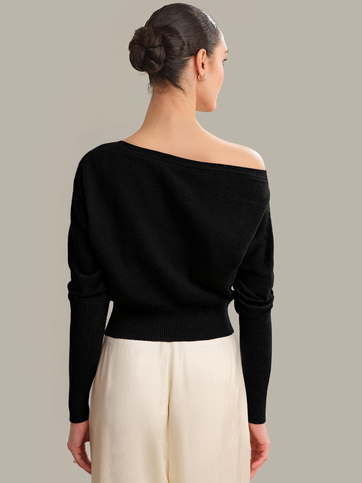 Woman wearing a black off-shoulder sweater and beige pants against a gray background