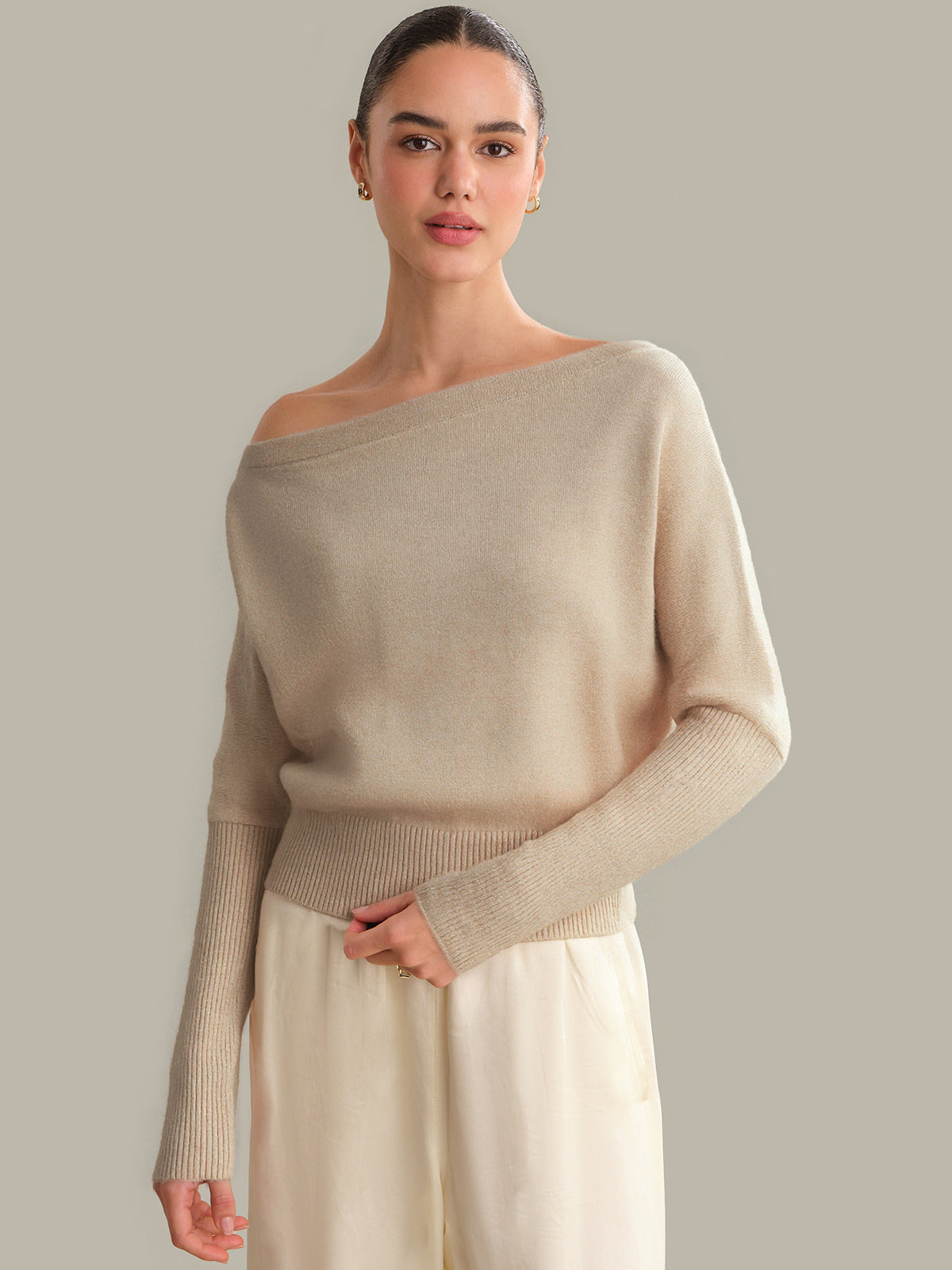 Woman wearing a beige off-shoulder sweater against a plain background