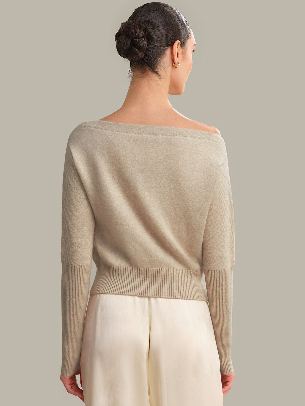 Woman wearing a beige sweater with a plain background