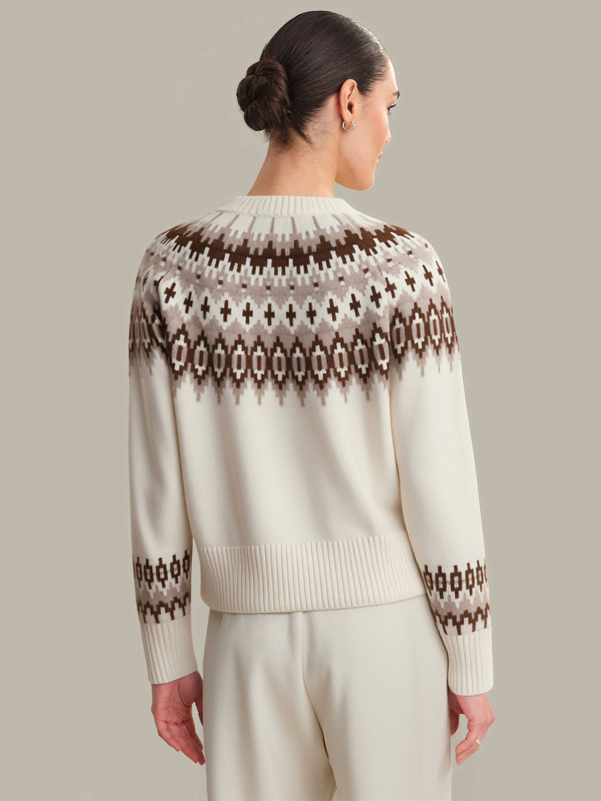 Woman wearing a cream sweater with a patterned back on a plain background