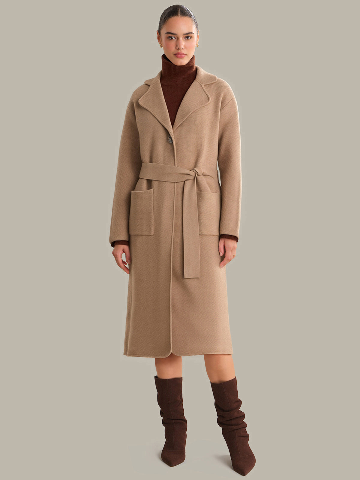 Woman wearing a beige coat with a belt on a gray background