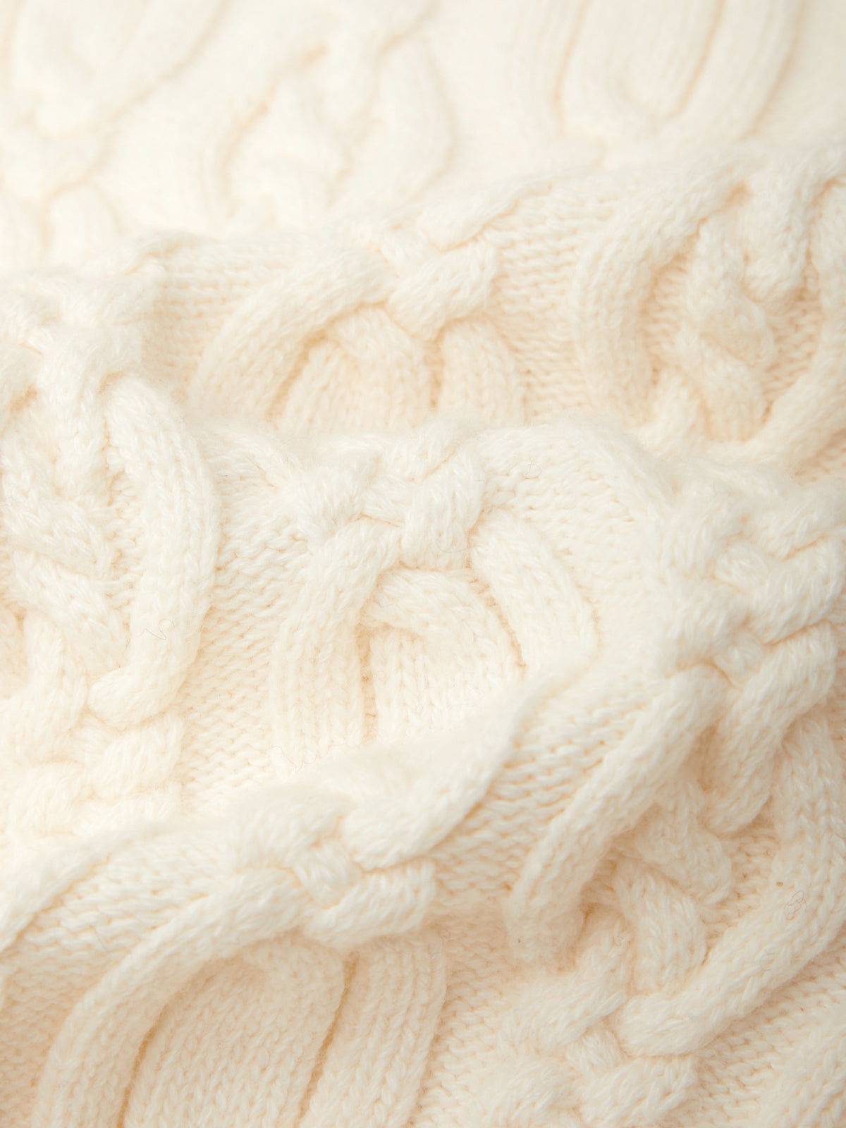 Close-up of a cream-colored cable-knit fabric with a thick, chunky texture.