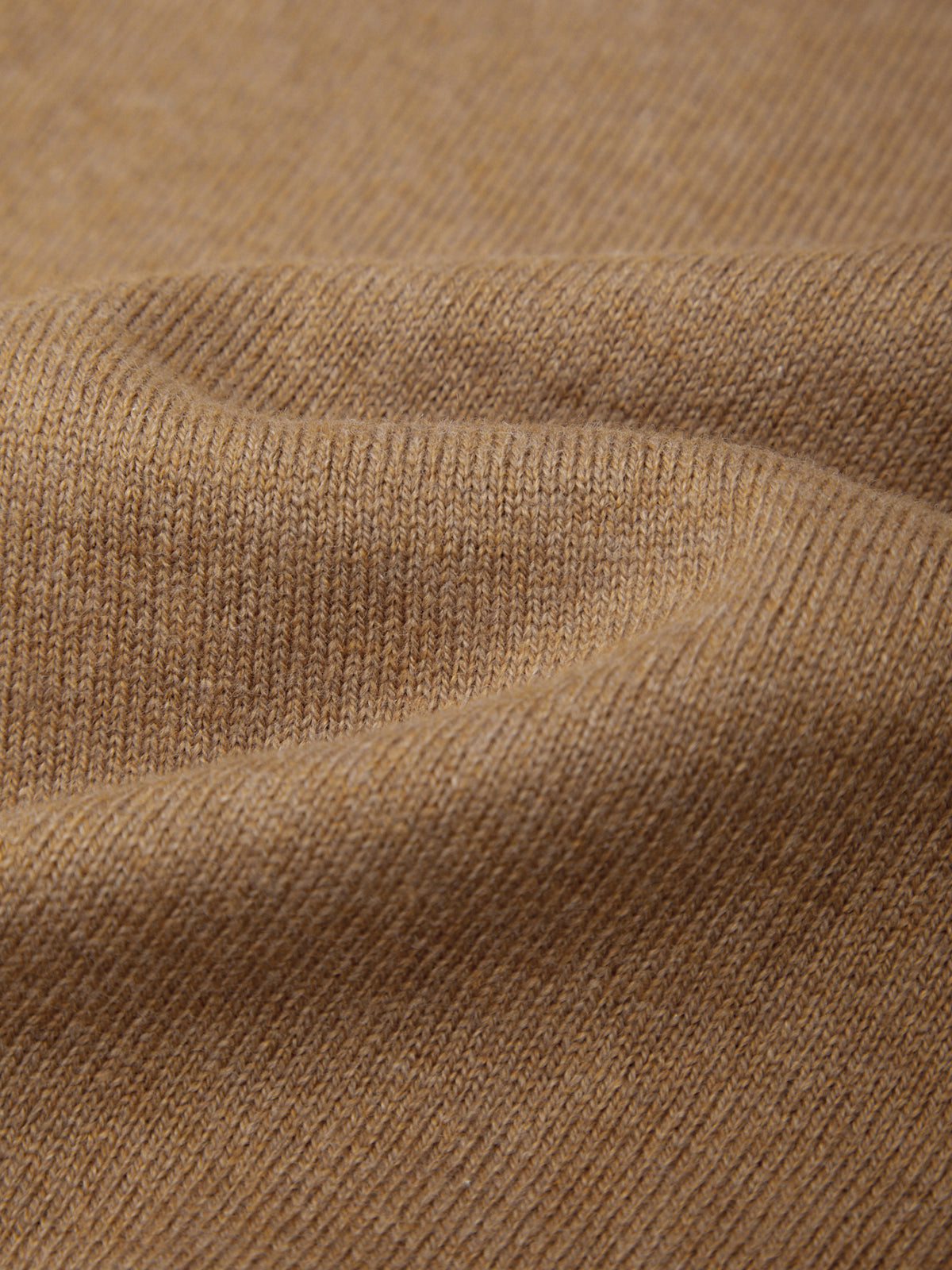 Close-up of a soft knit fabric in a warm camel tan color, showing the fine ribbed texture and gentle folds.