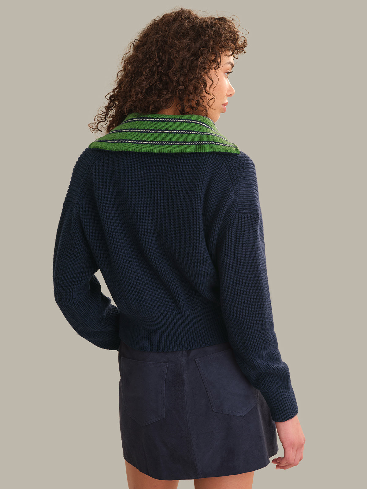 A model shown from the back wearing a navy blue ribbed knit sweater with a green striped collar, paired with a matching navy mini skirt, against a solid light gray background.