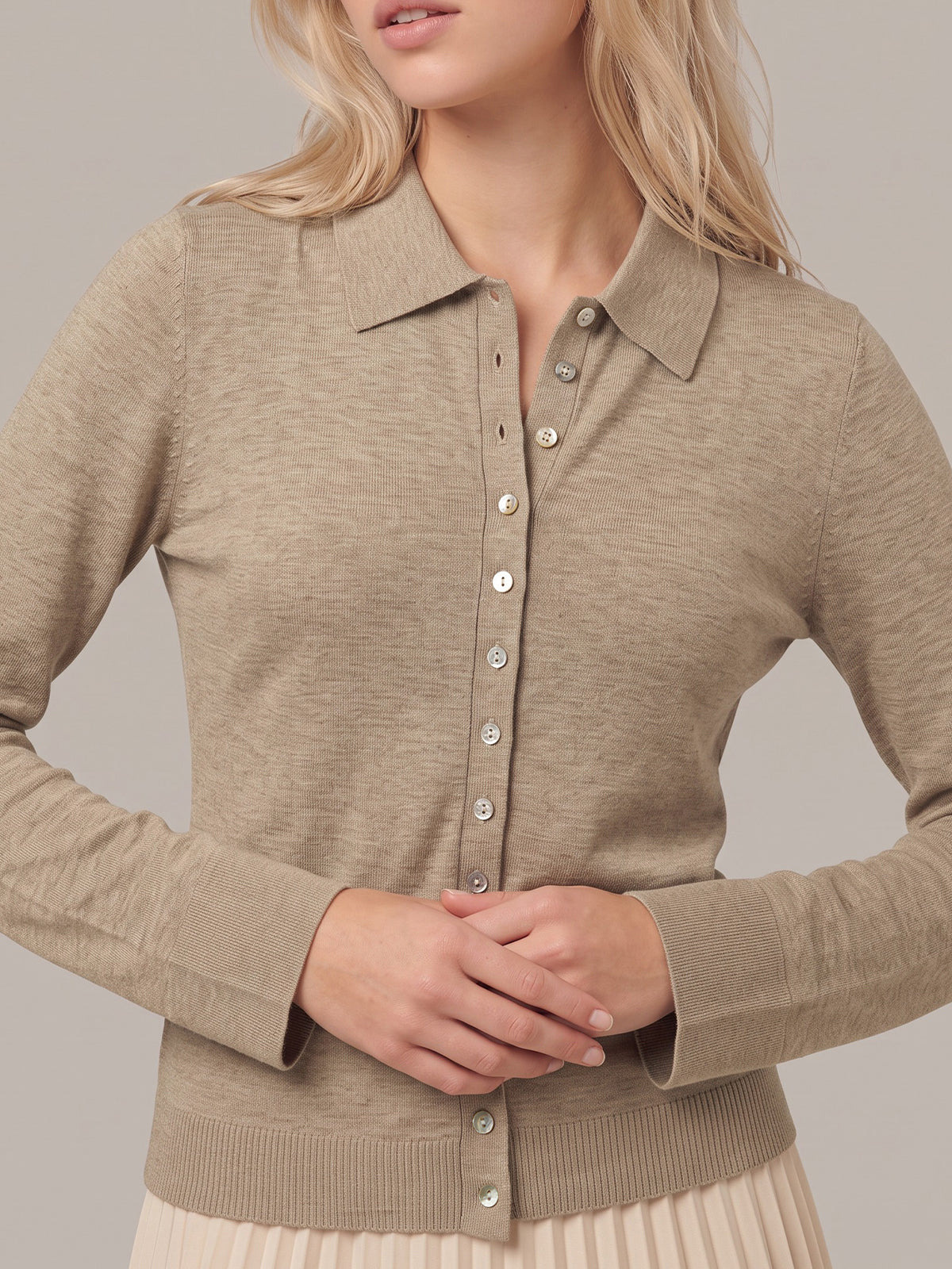 A woman wearing a taupe-beige long-sleeve knit polo-style cardigan with a button front, shown from the shoulders to the hips against a plain light gray studio background.