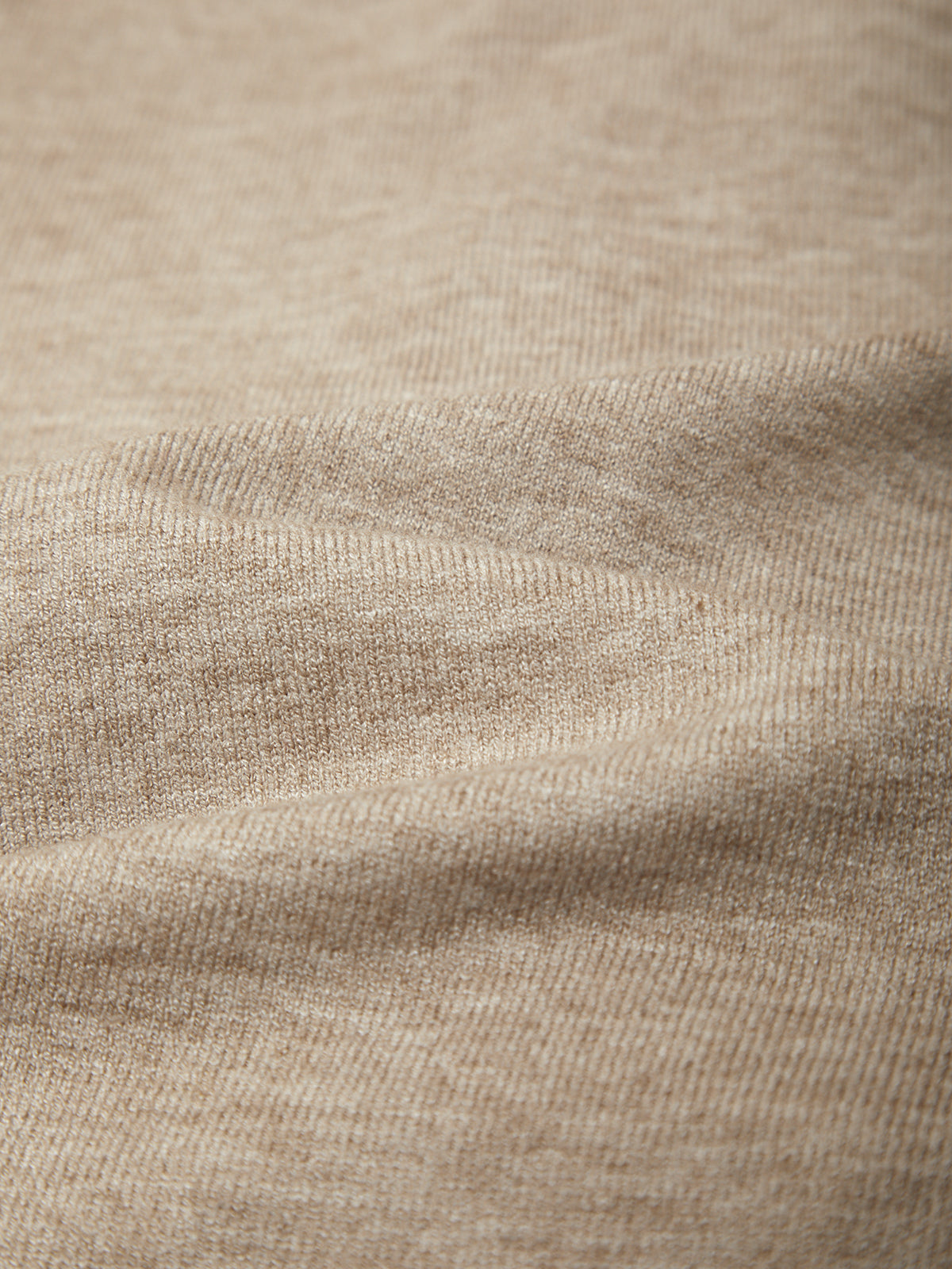 A close-up of a soft knit fabric in a warm light beige or oatmeal tone, showing the texture and weave with gentle folds.