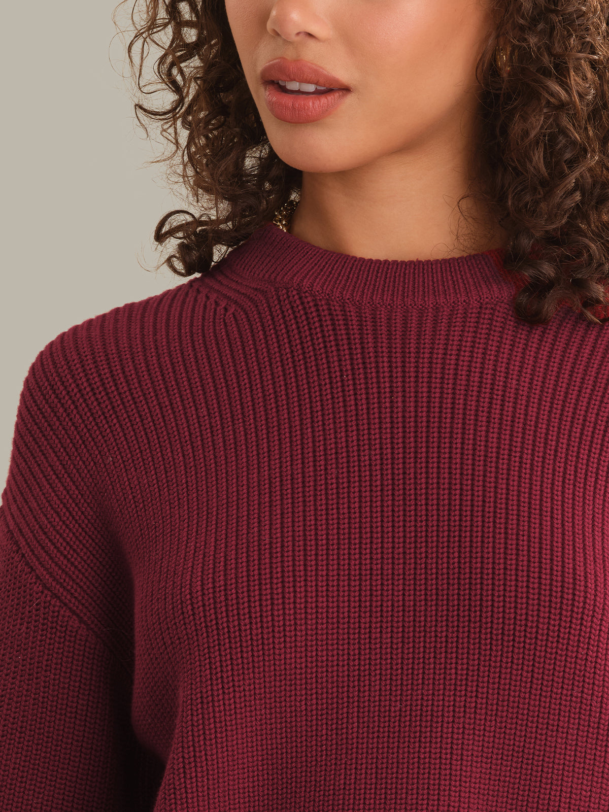 Close-up of a woman wearing a ribbed knit sweater in deep burgundy, showing the texture of the fabric and the crew neckline.