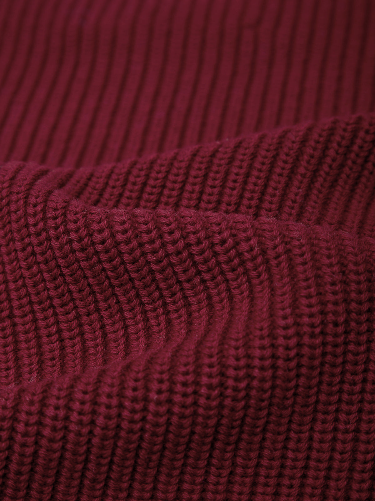 Close-up of a dark burgundy ribbed knit fabric texture, showing the detailed knit pattern and folds.
