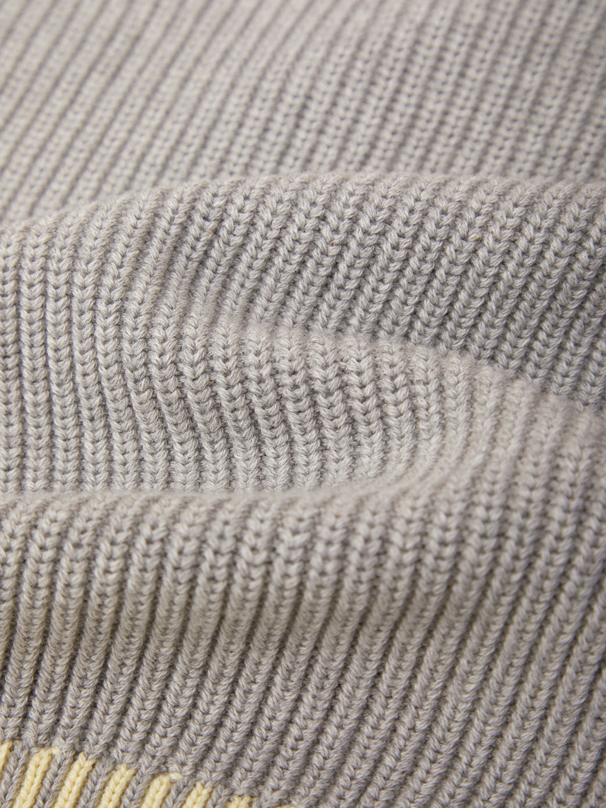 Close-up of a ribbed knit fabric in a light warm gray or taupe color, showing the texture and stitch pattern.