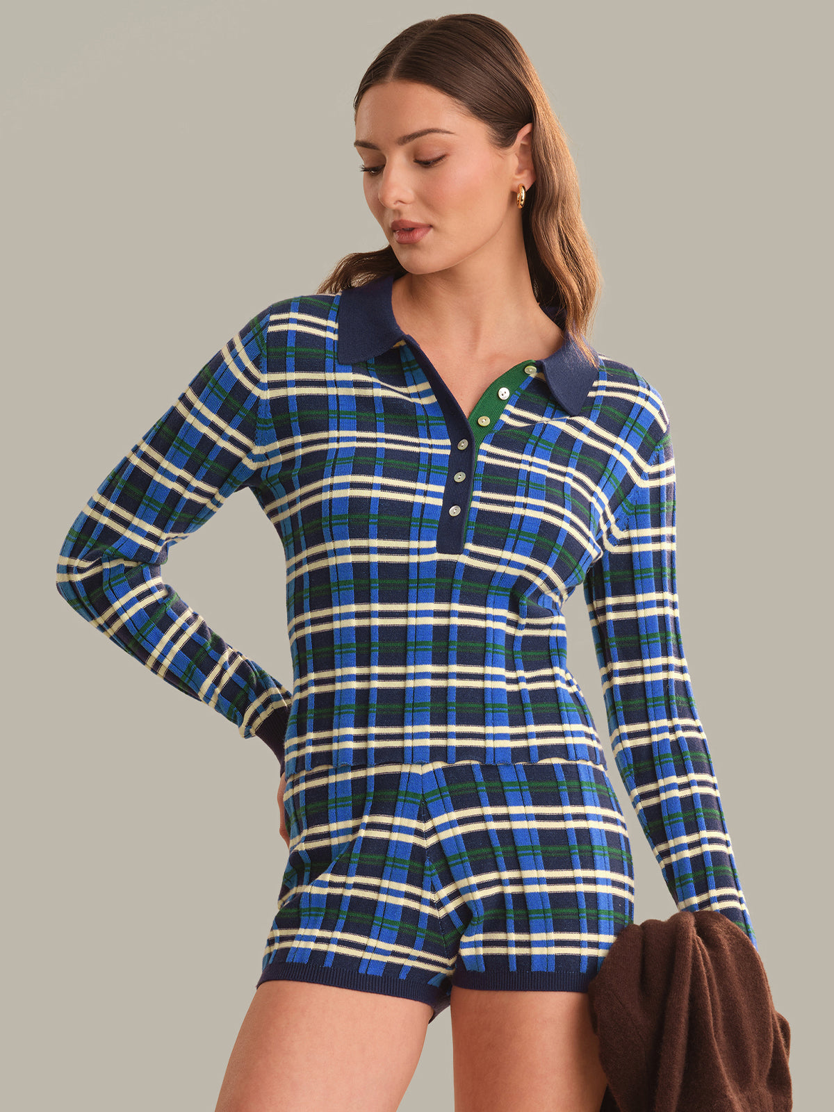 A woman wearing a long-sleeve plaid polo top with matching plaid shorts, featuring a blue, green, and white tartan pattern with a dark blue collar and green button detail.