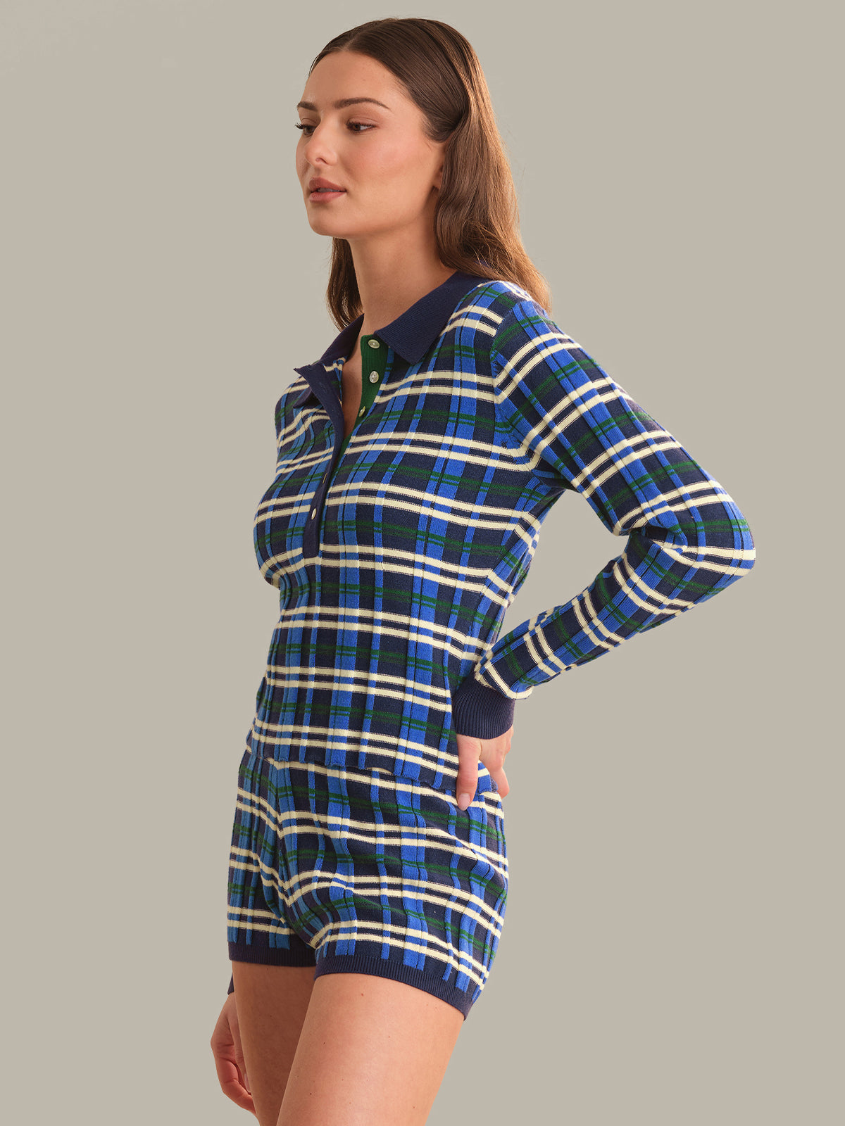 A woman modeling a long-sleeve plaid top and matching plaid shorts in blue, navy, and white, featuring a half-button collar, set against a solid gray background.