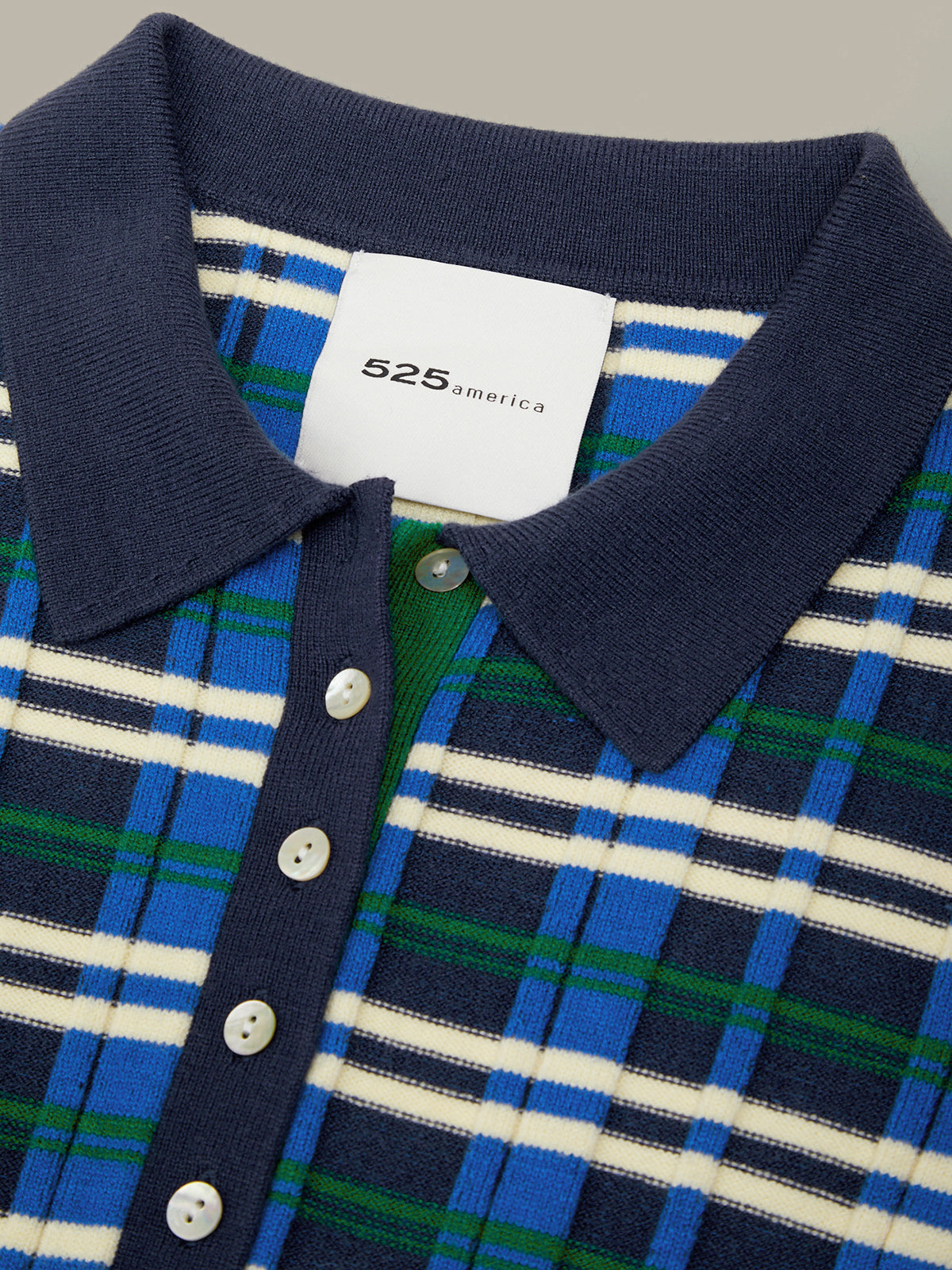 Close-up of a knit polo shirt collar and button placket showing a blue, green, and white plaid pattern with a white 525america brand label.