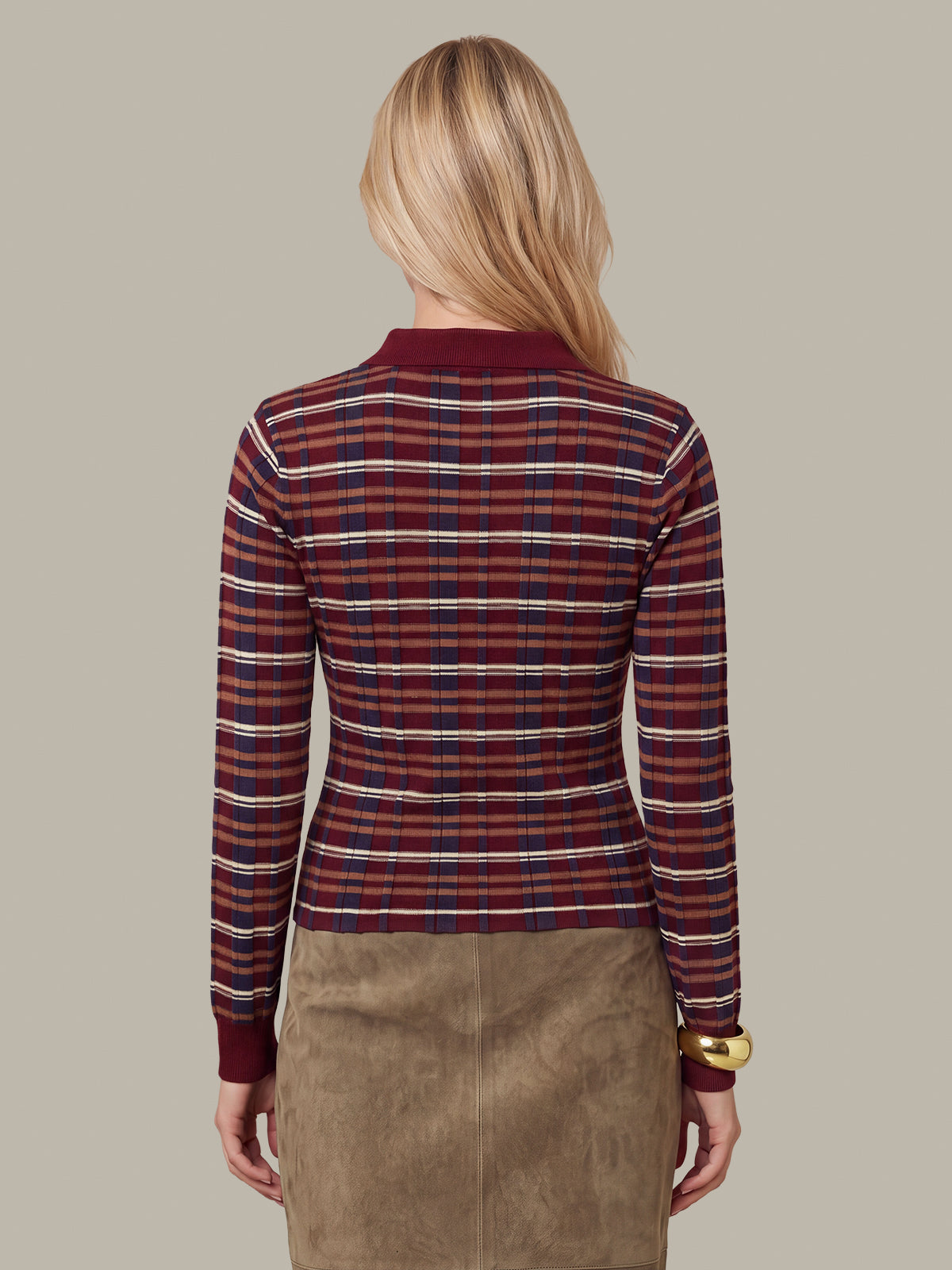 A woman shown from the back wearing a long-sleeve plaid knit top with red, navy, and white stripes, paired with a brown skirt, against a solid beige background.