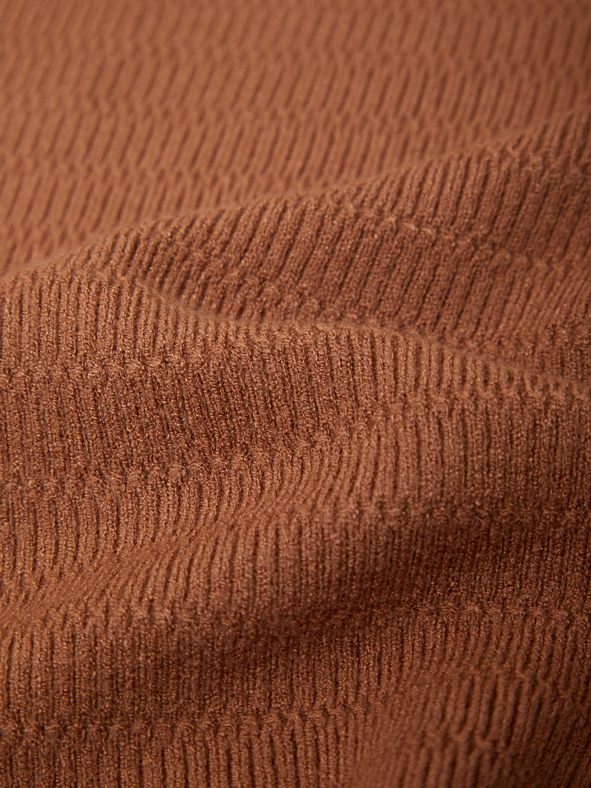 Close-up of a ribbed knit fabric in a warm rust brown color, showing the texture and folds of the material.