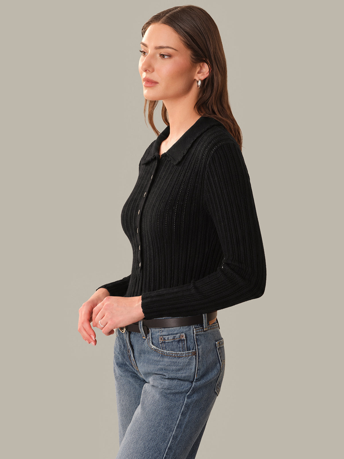 Woman wearing a black ribbed sweater and blue jeans against a gray background