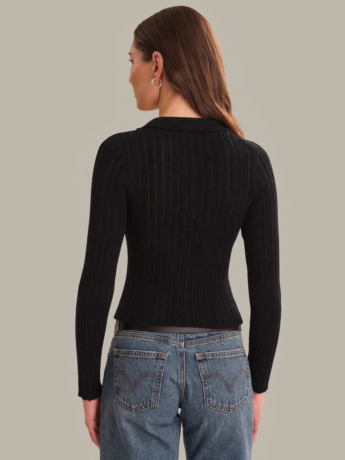 Person wearing a black ribbed sweater and blue jeans on a plain background