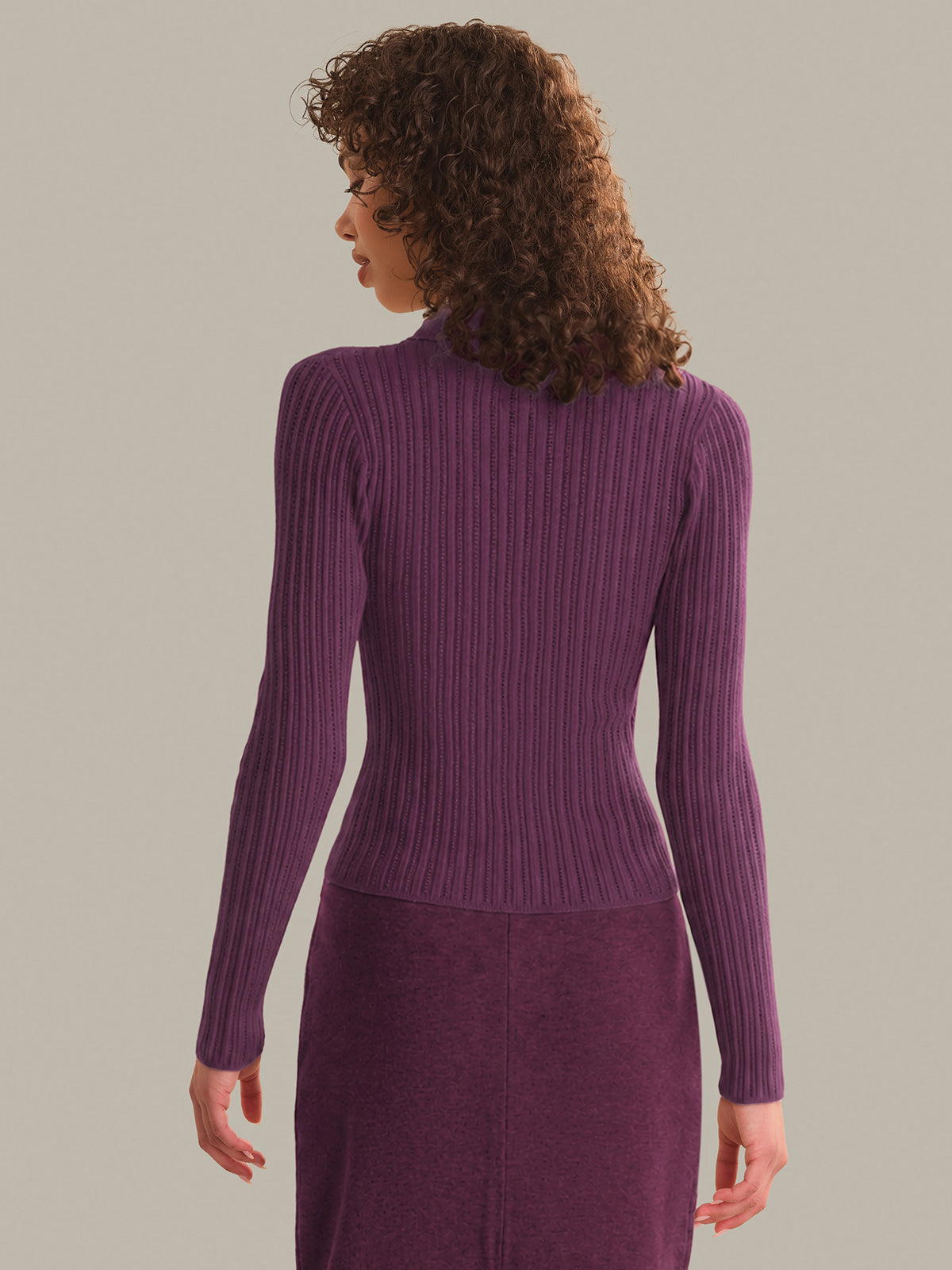 Woman wearing a purple ribbed sweater and skirt set against a plain background