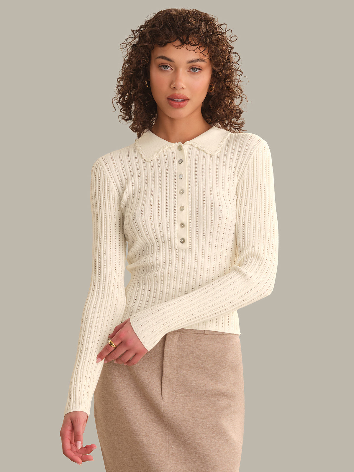 Woman wearing a cream ribbed sweater over a beige shirt with a plain background