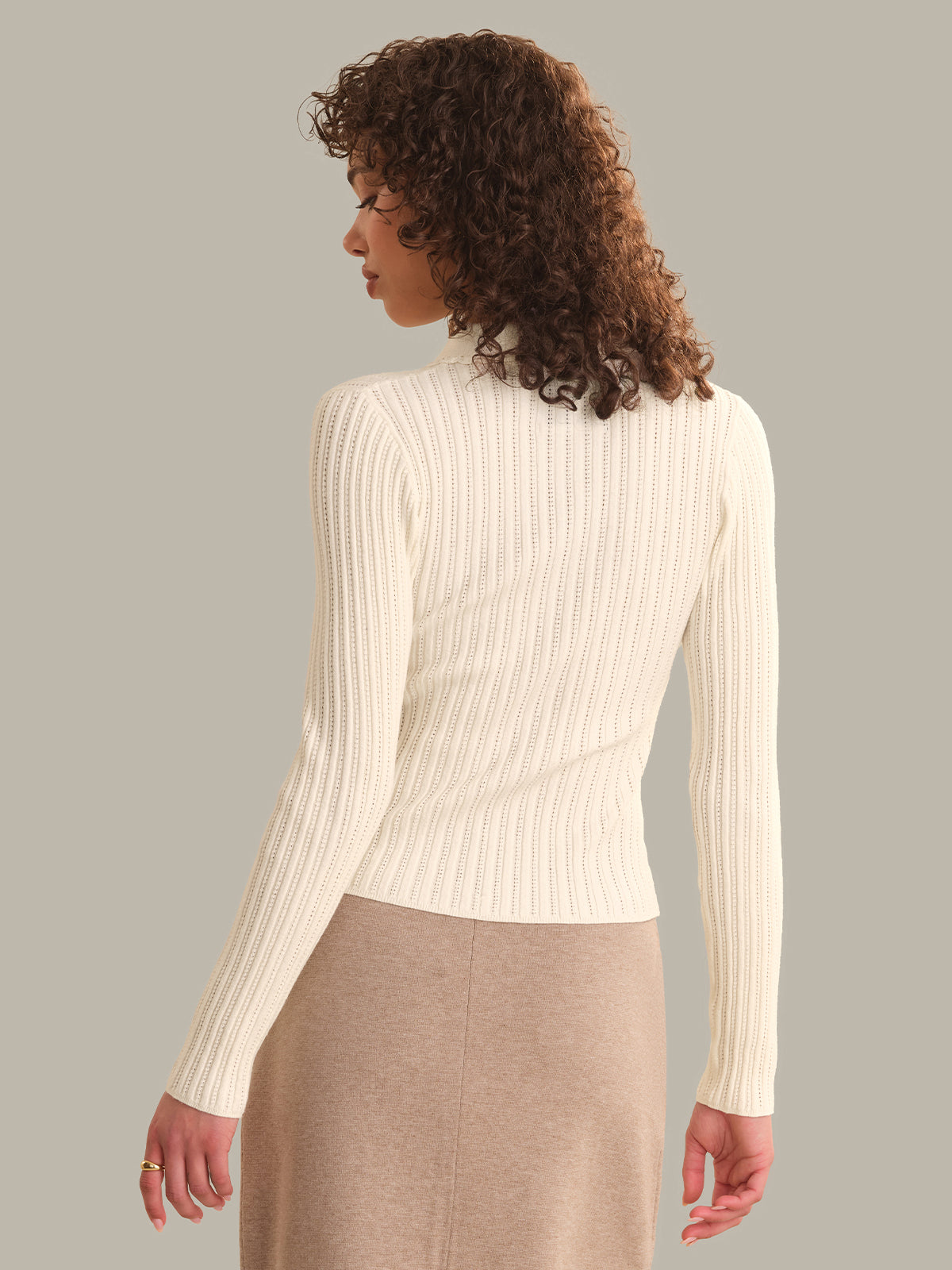 Woman wearing a cream ribbed sweater against a gray background