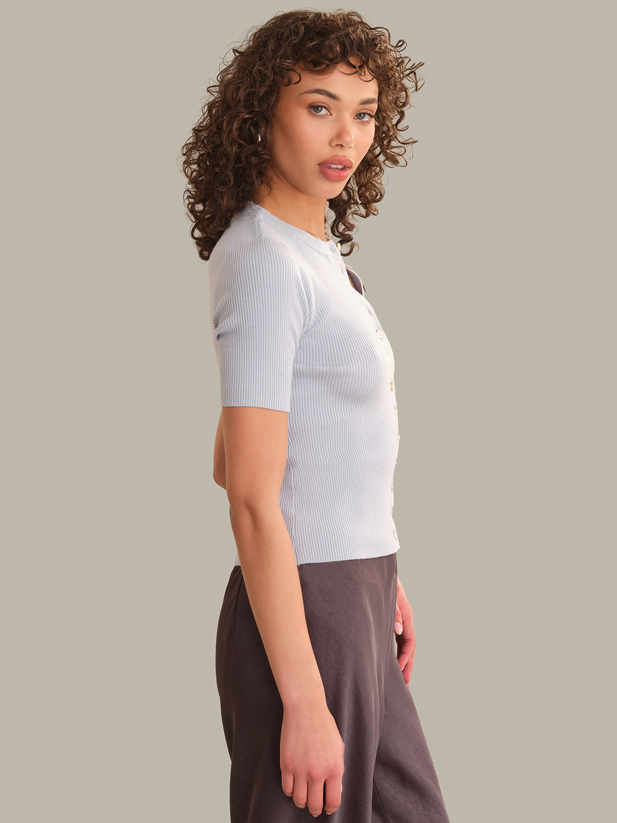 Woman wearing a light blue top and dark pants against a plain background