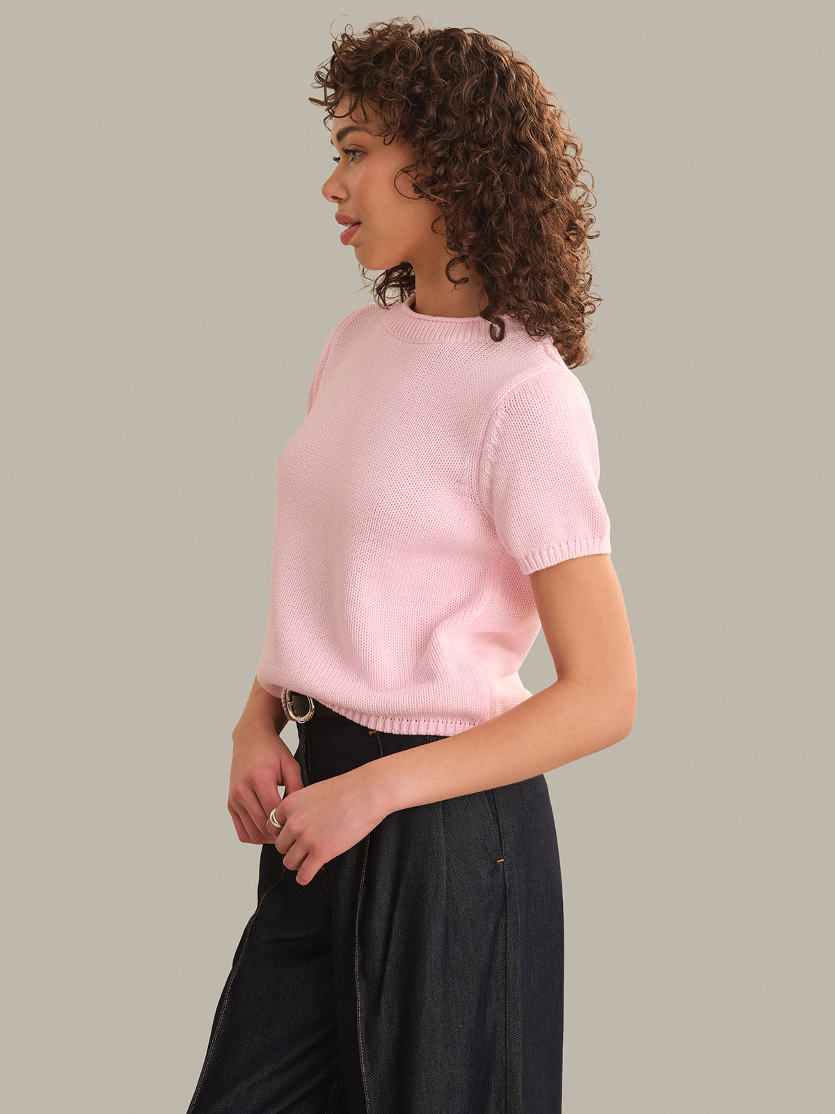 Person wearing a light pink sweater and dark pants on a neutral background