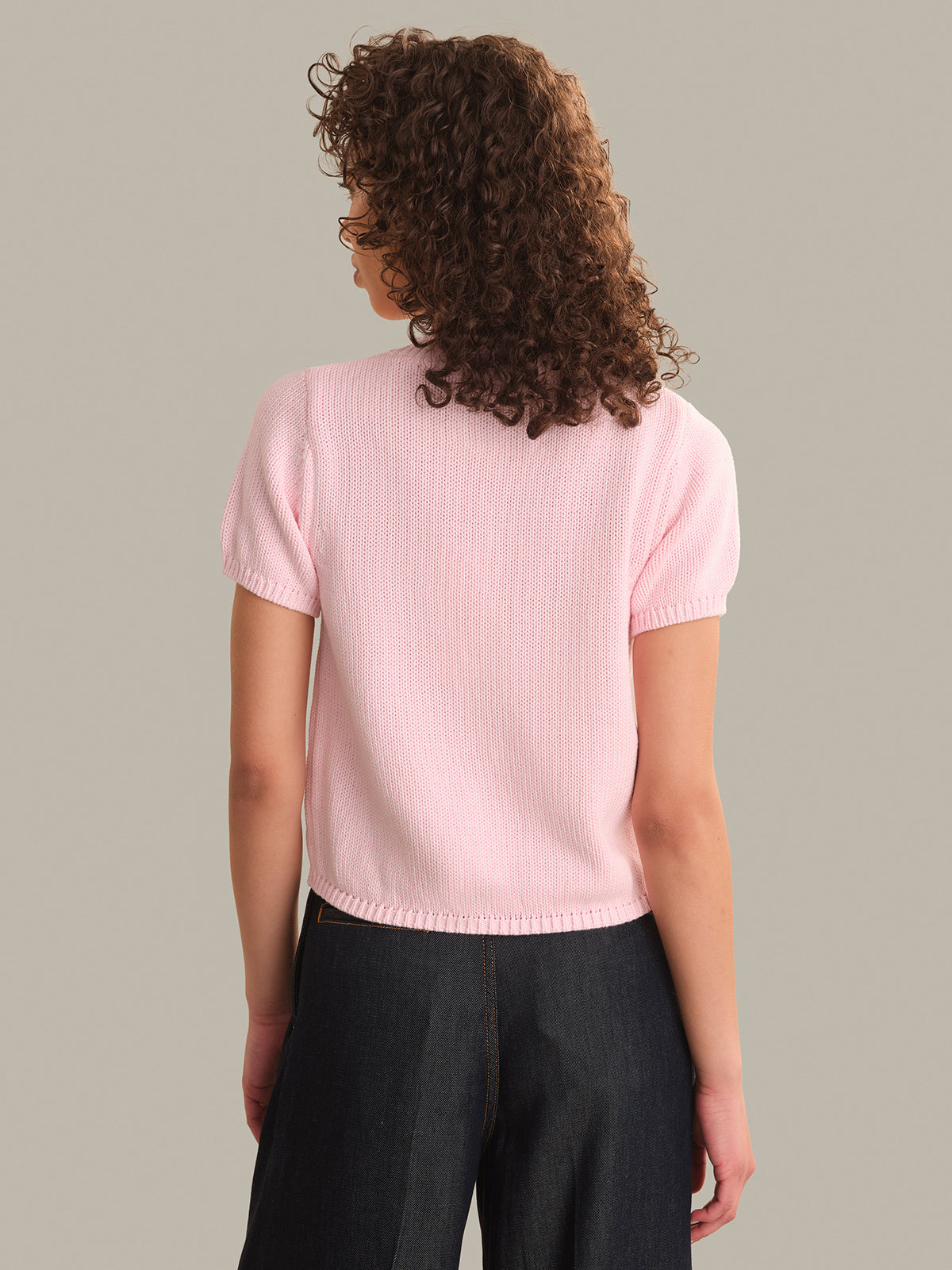 Person wearing a light pink short-sleeve sweater against a neutral background