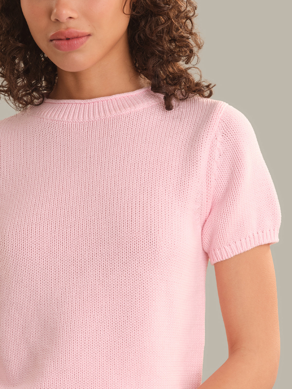 Person wearing a light pink knitted sweater against a neutral background