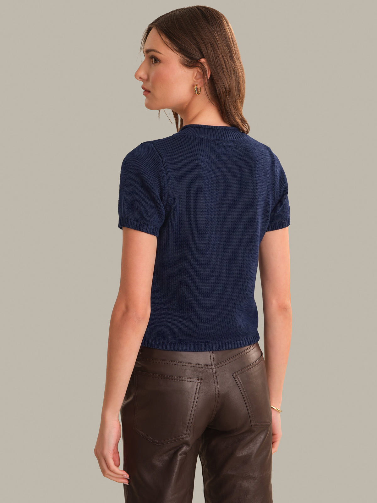 A woman shown from the back wearing a navy blue short-sleeve ribbed knit top and dark brown pants, photographed against a plain light gray studio background.