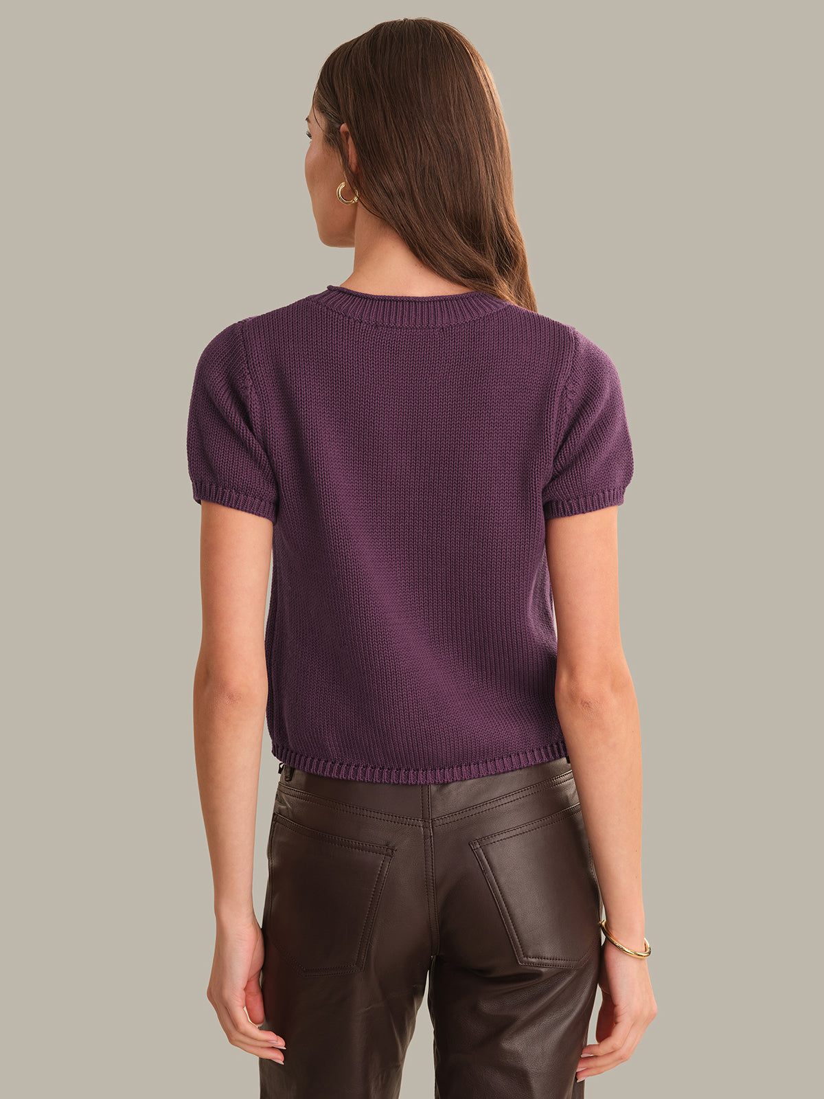 Person wearing a purple sweater and brown pants on a neutral background